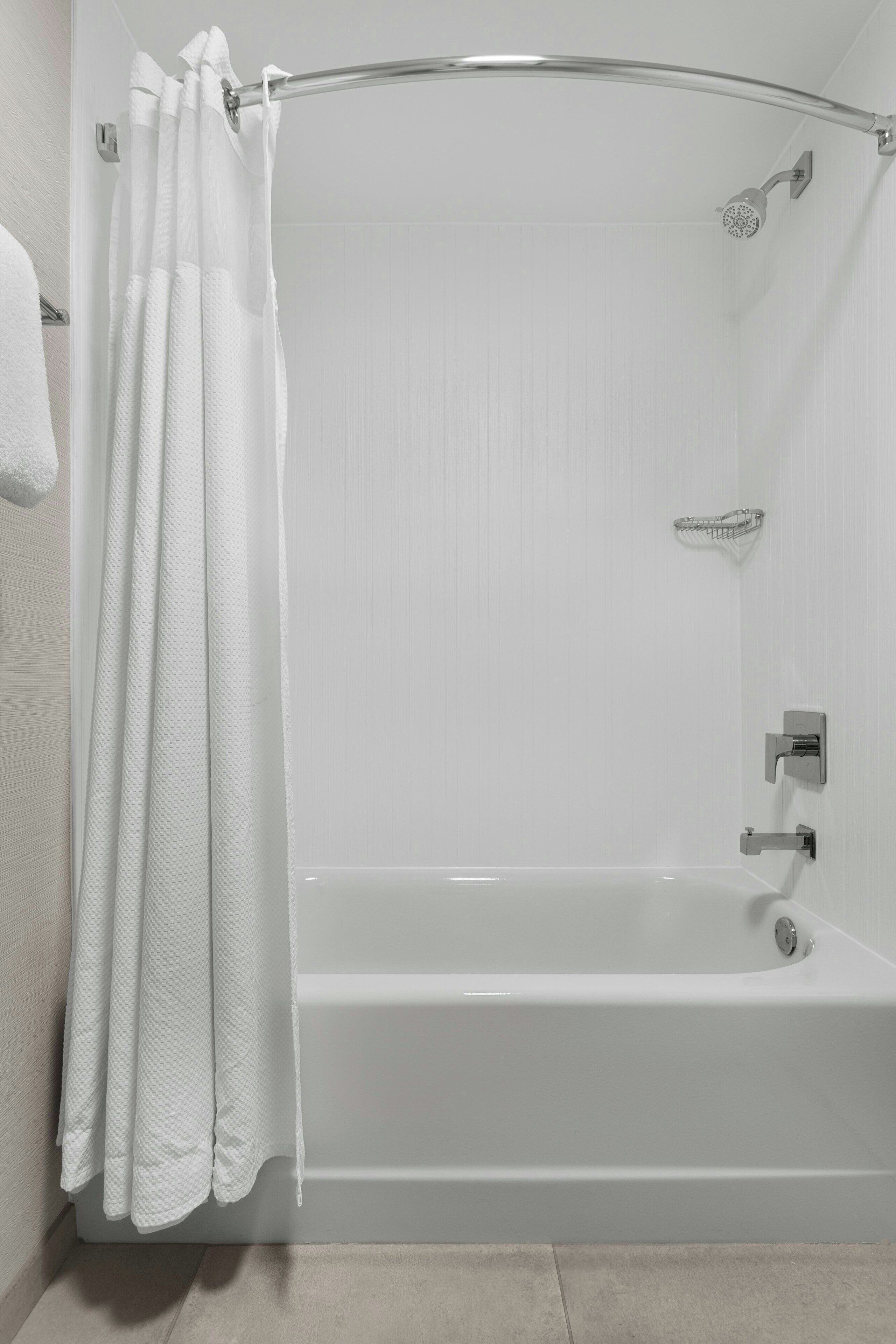 A modern bathroom with a white bathtub, shower, and curtain.