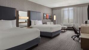 A hotel room with two beds, a desk, a chair, a lamp, and a large window with curtains. - Courtyard by Marriott Louisville Airport (Louisville)