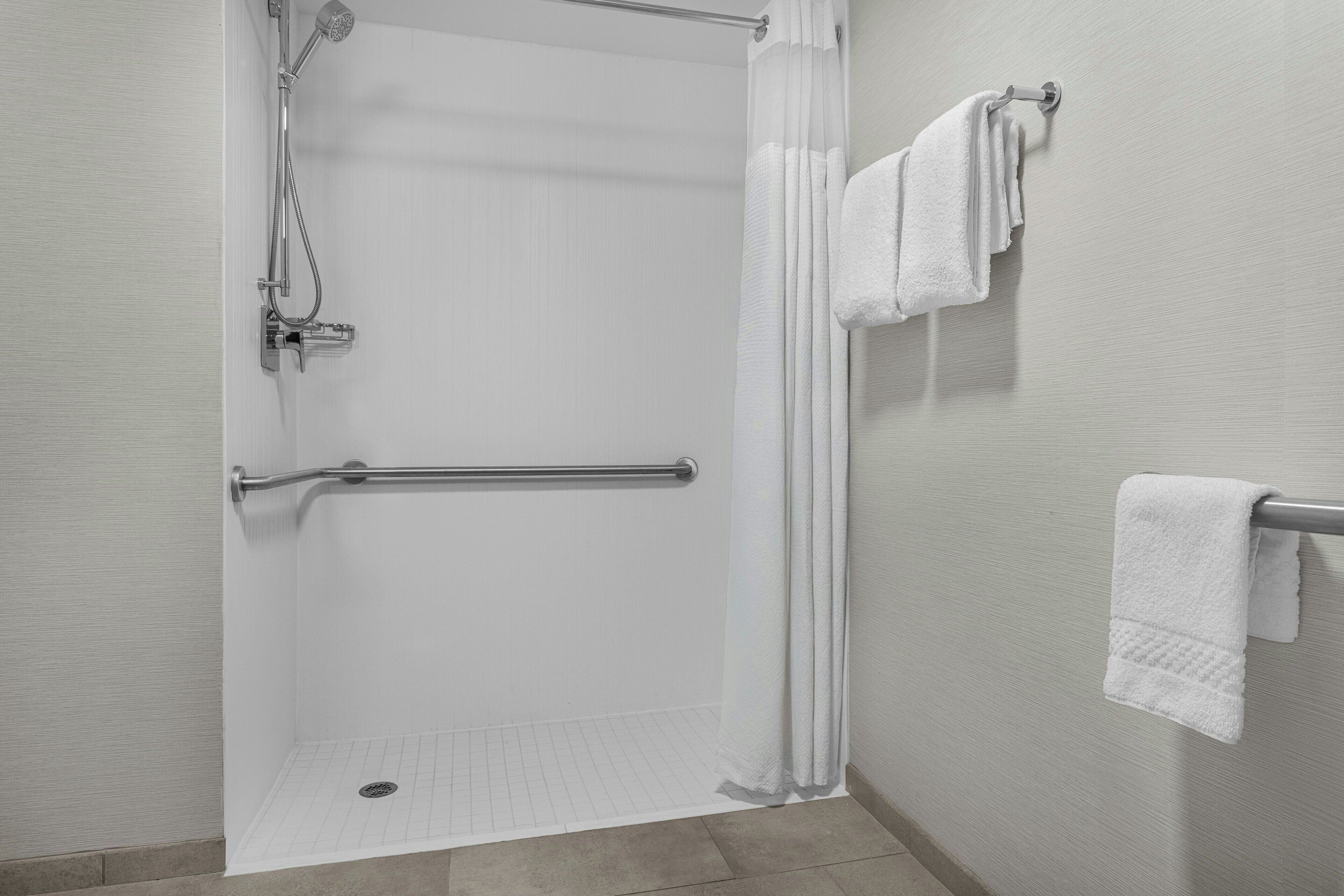 A shower area with a grab bar, a towel rack with multiple towels, and a showerhead.