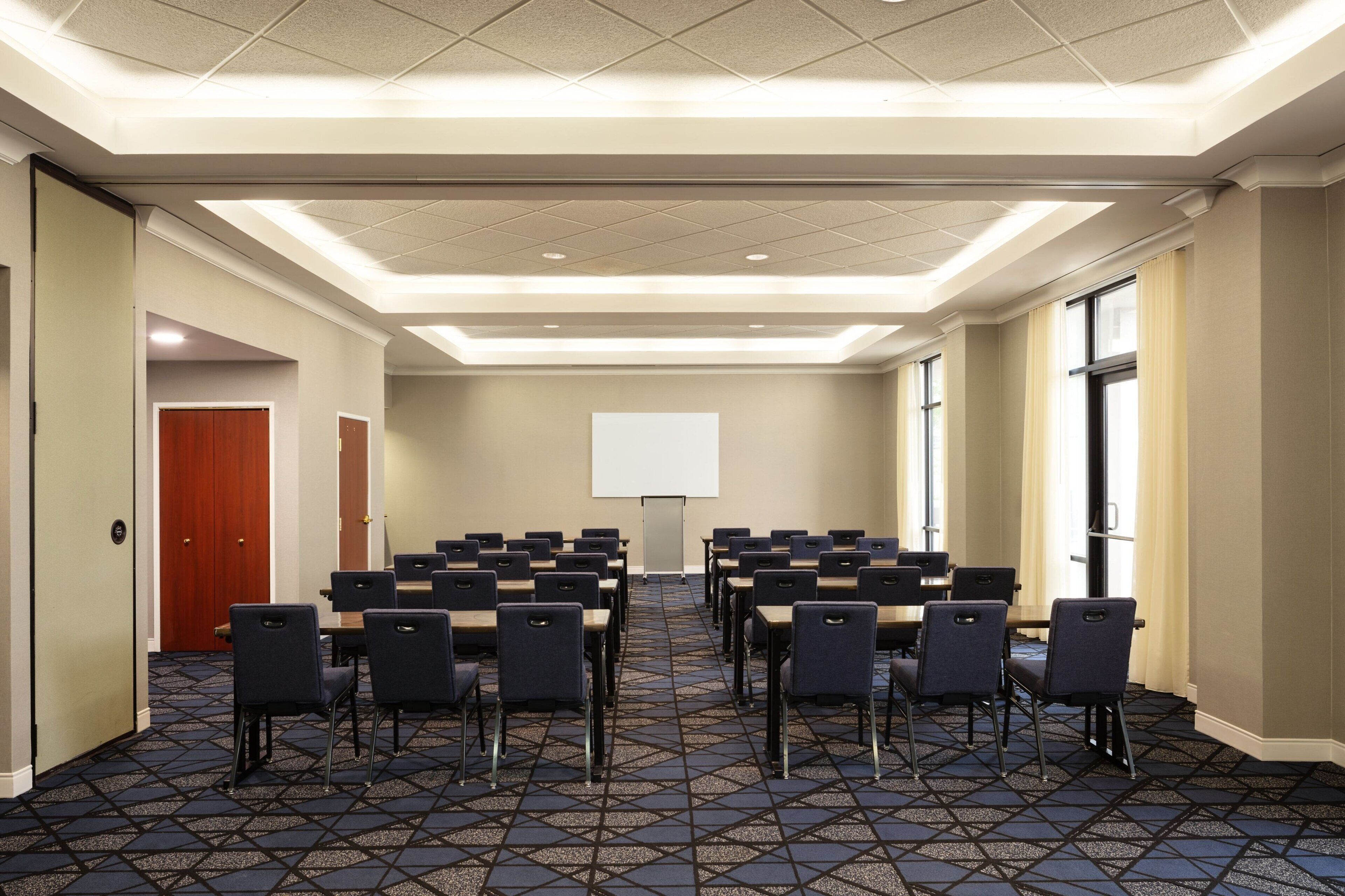 A conference room with a large screen, rows of tables and chairs, and a patterned carpet.