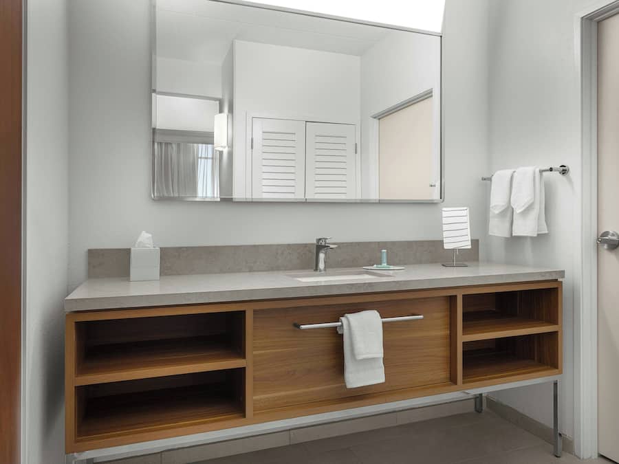 A modern bathroom with a wooden vanity, a large mirror, and a towel rack.