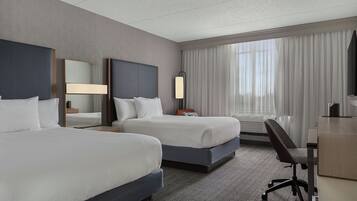 A hotel room with two beds, a desk, a chair, a large mirror, and a window with curtains.