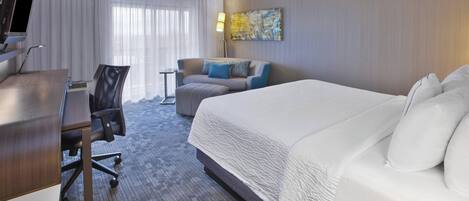 Habitación de hotel con una cama grande, un escritorio con computadora, un sofá y un cuadro en la pared.