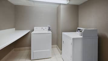 A laundry room with two white washers and dryers, a white shelf, and a tiled floor.