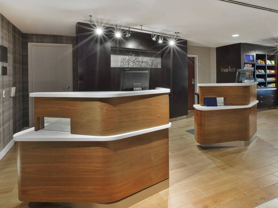 A reception area with wooden reception desks, a digital screen, and a refrigerator stocked with beverages.