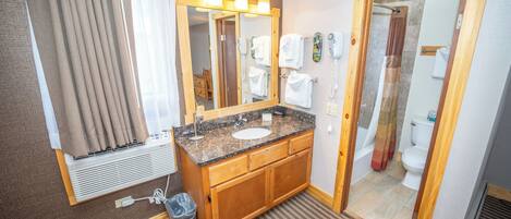 A hotel bathroom with a wooden vanity, a sink, a mirror, and a shower area.