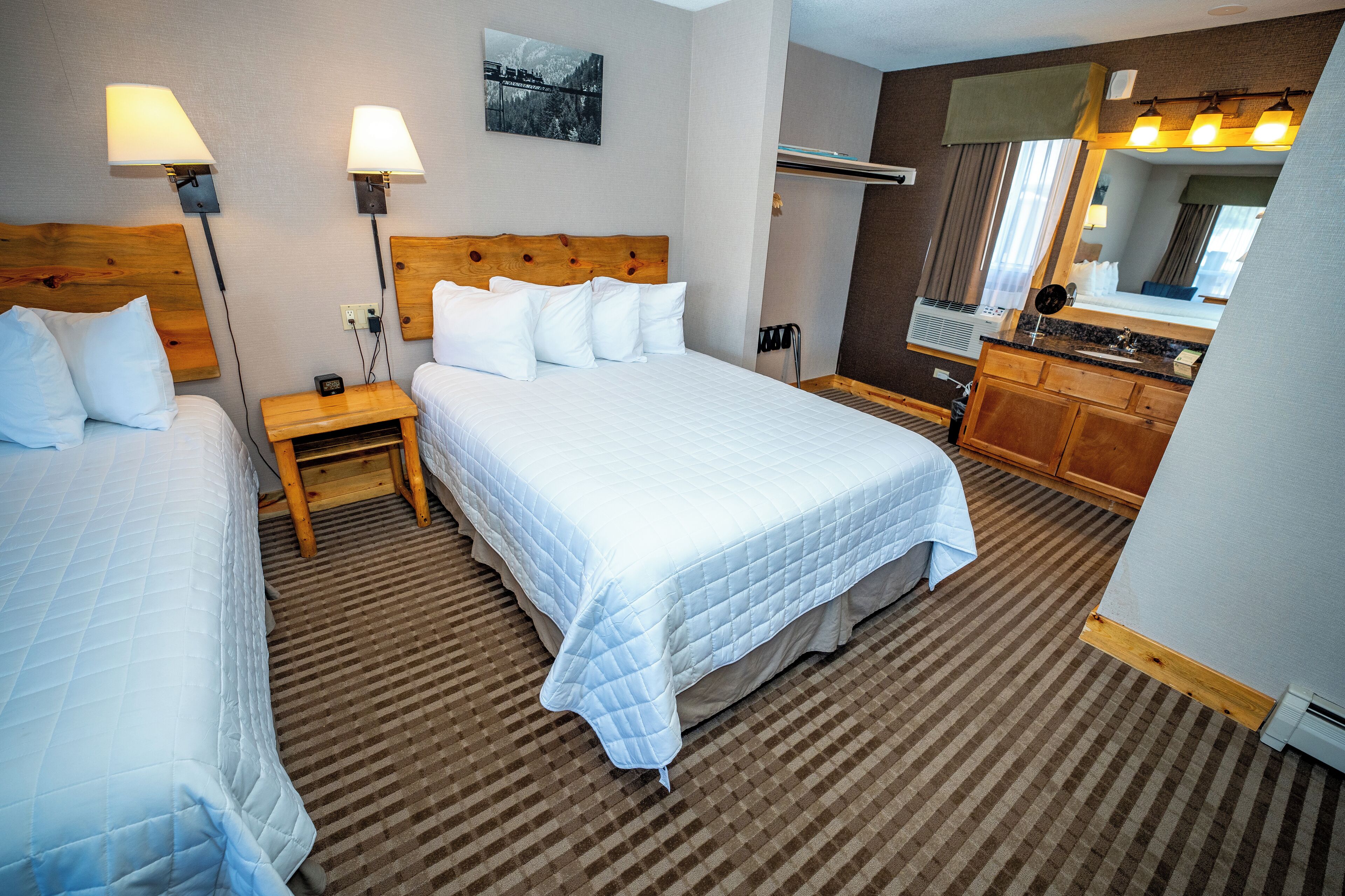 Een hotelkamer met twee bedden, een houten hoofdbord, een nachtkastje, een spiegel, een wastafel en een raam met gordijnen.