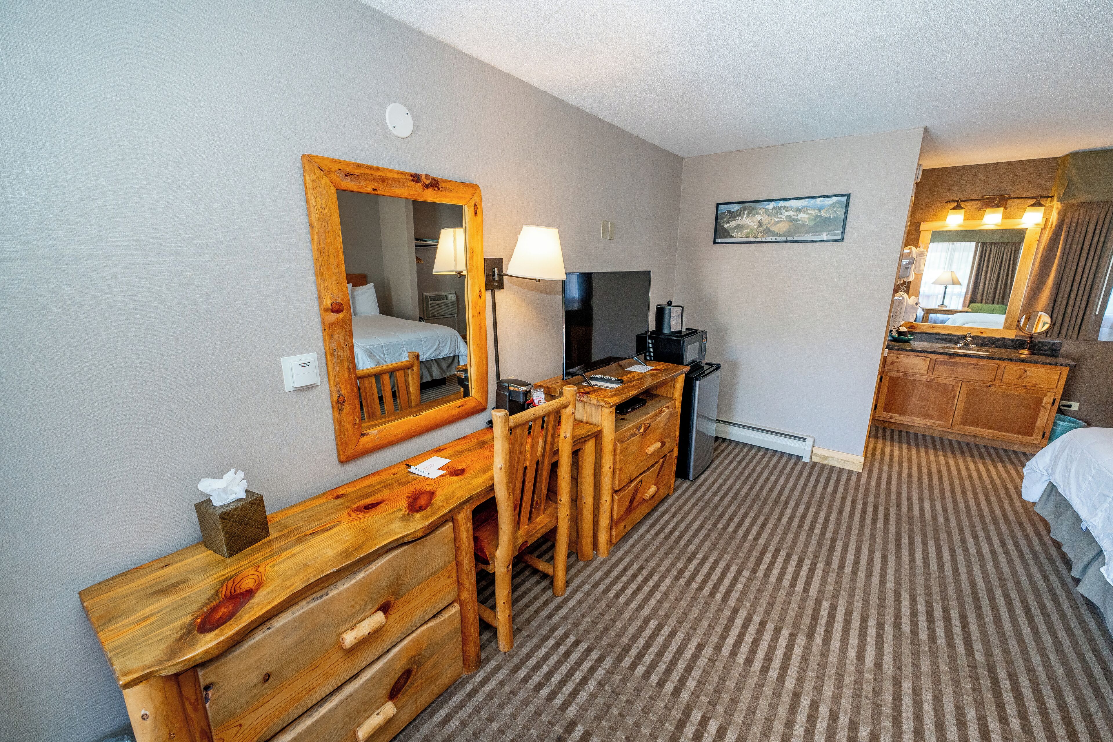 A hotel room with a wooden desk, a chair, a television, a lamp, and a bed.