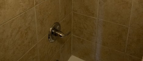 Un área de ducha con cabezal de ducha de mano, grifo empotrado en la pared y lavamanos en esquina.