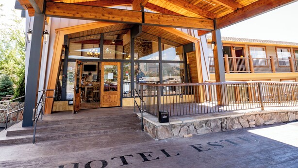 A wooden covered entrance to a hotel with a stone base and a sign reading "HOTEL ESTEL". - Hotel Estes (Estes Park)
