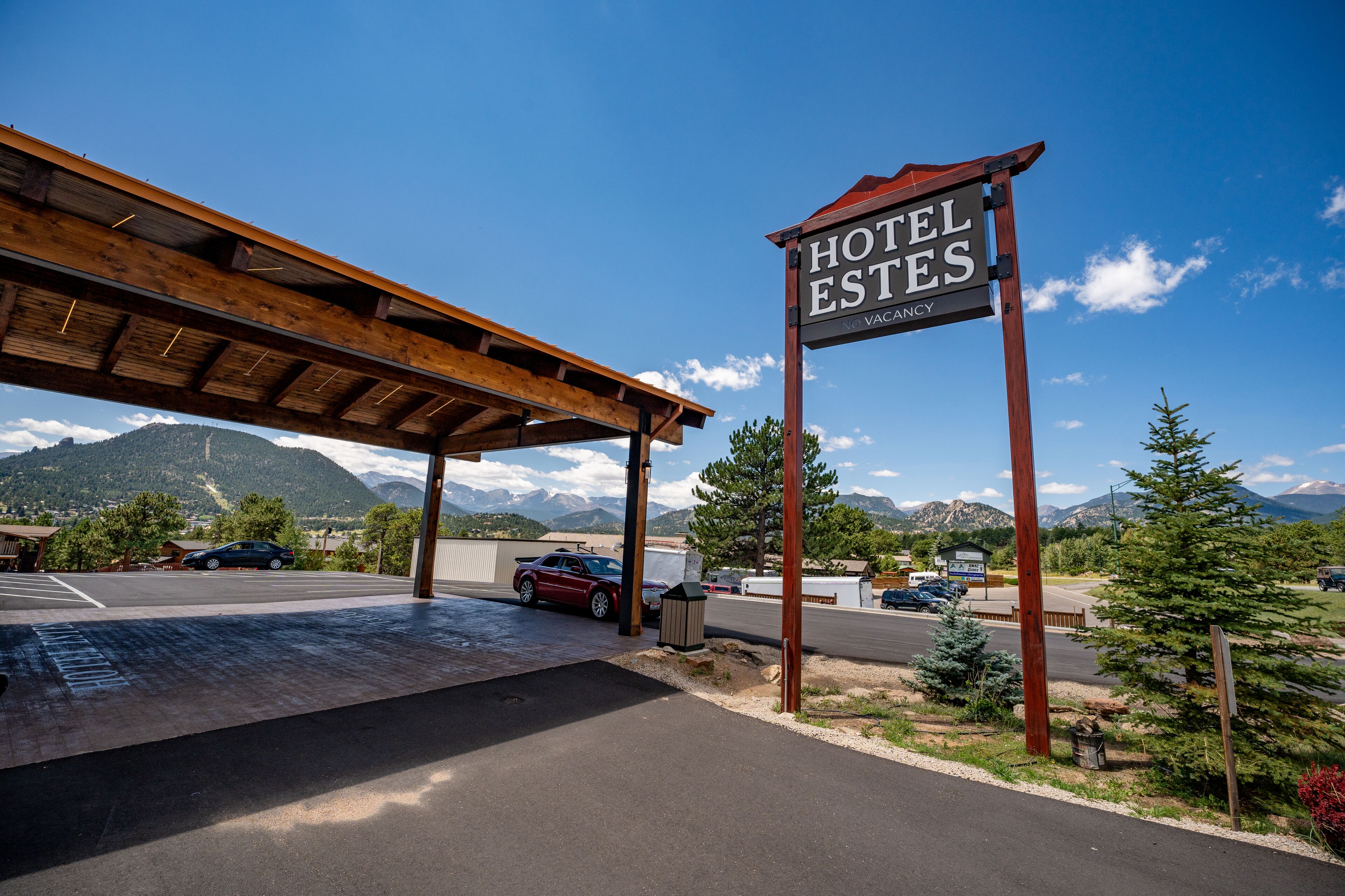 A hotel entrance with a covered parking area, a sign indicating 'Hotel Estes', and a mountainous backdrop.