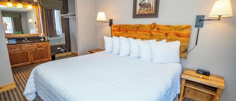 A hotel room with a large bed, a wooden headboard, a mirror, a vanity with a sink, and two bedside lamps.