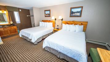 A hotel room with two beds, a wooden headboard, a green bench, a wooden dresser, and a large mirror.