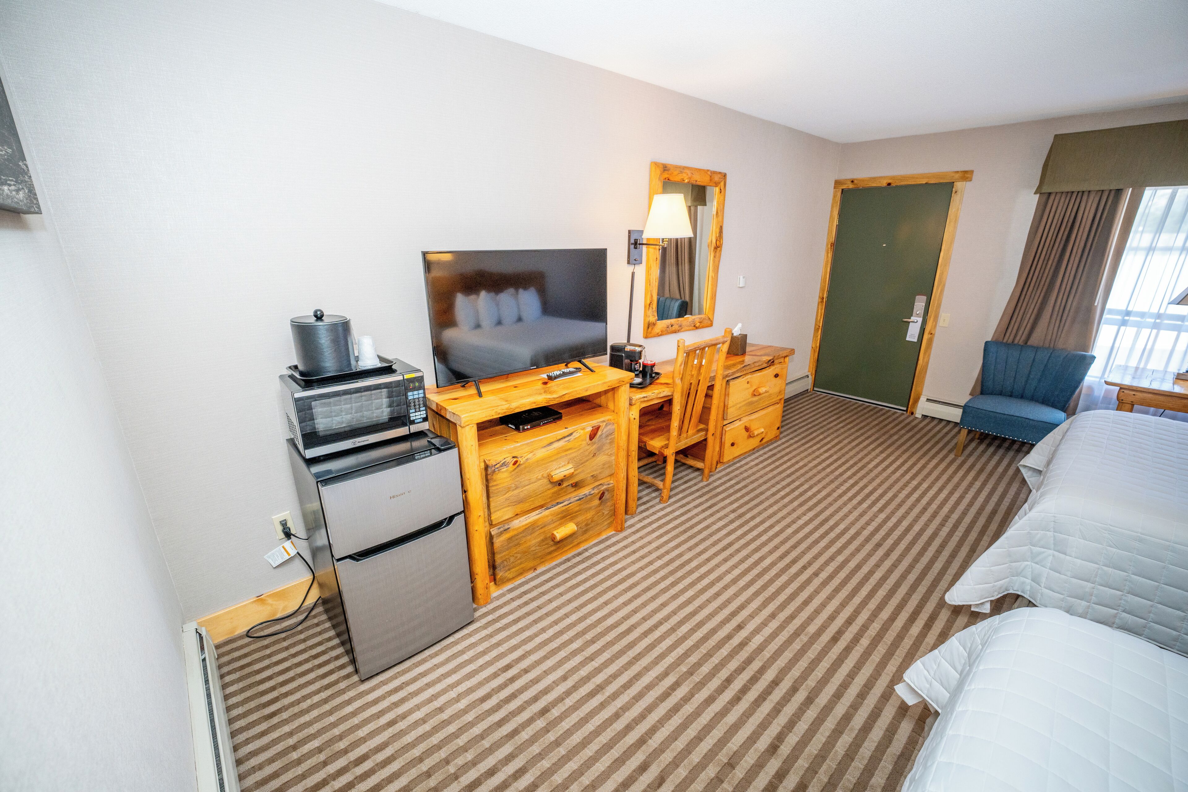 Une chambre d’hôtel comprenant un lit, un bureau avec une télévision, un réfrigérateur, un miroir et une porte.