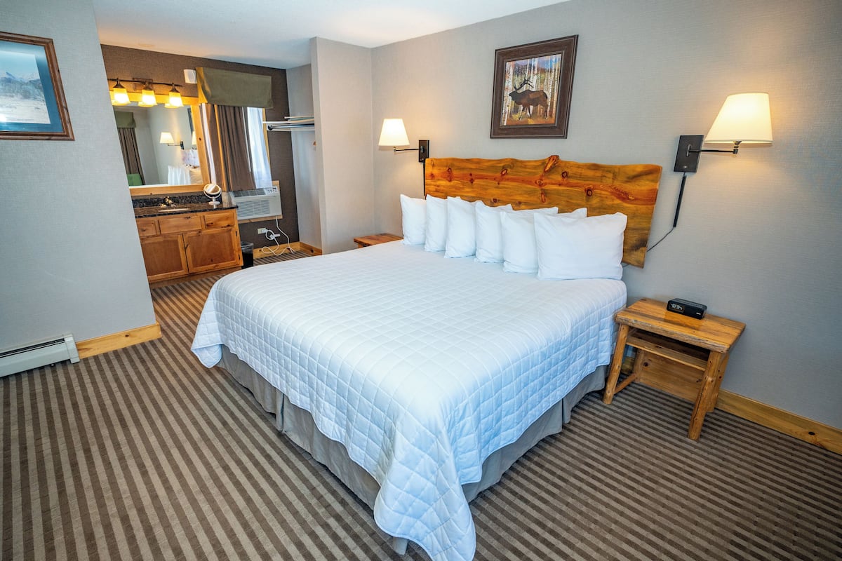 A hotel room with a large bed, a wooden headboard, two bedside lamps, a nightstand, a dresser, a mirror, and a framed picture on the wall.