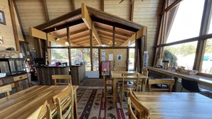 A rustic wooden interior with a central dining area, wooden tables and chairs, a kitchen area with a counter, and large windows providing natural light. - Hotel Estes (Estes Park)