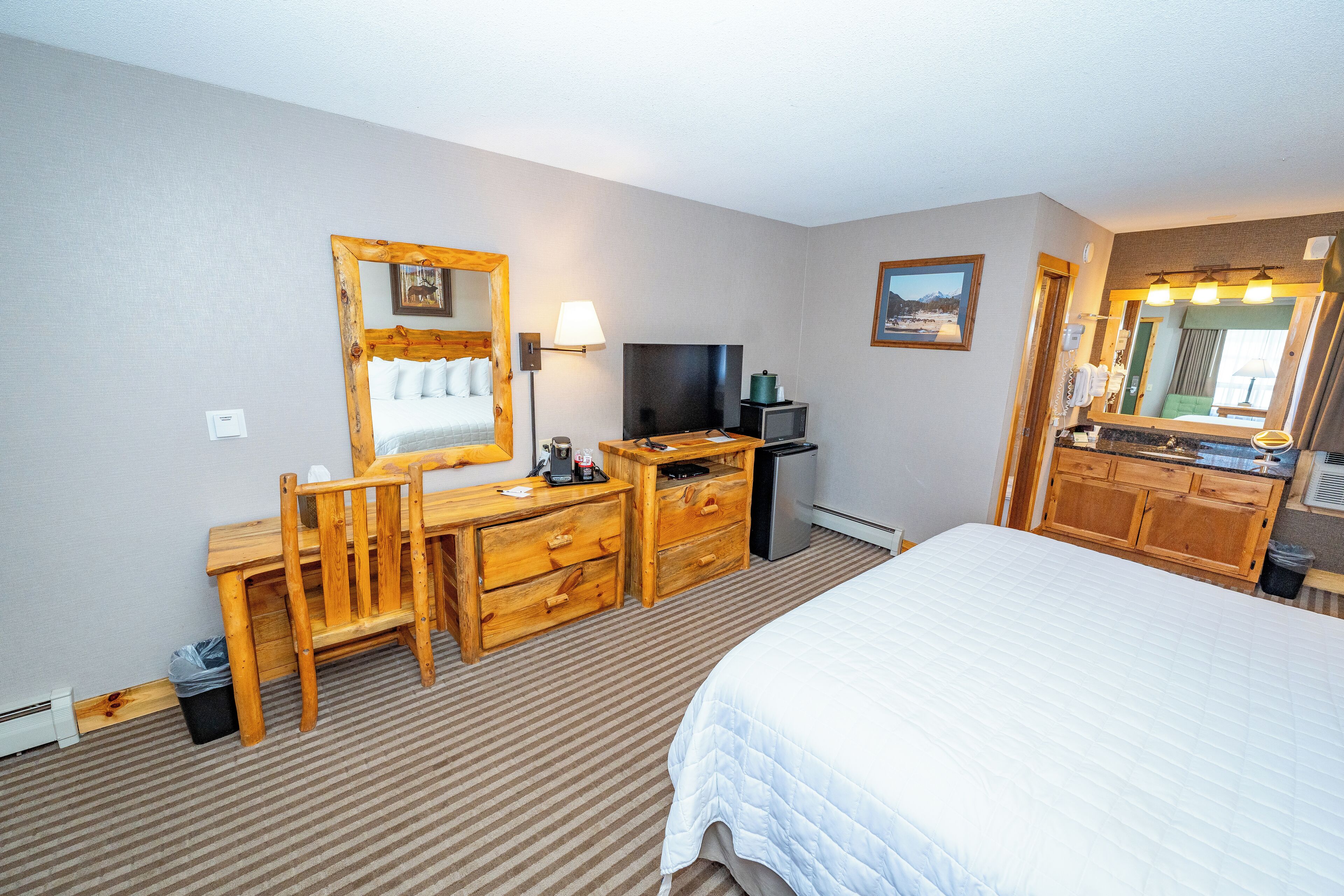 A hotel room with a bed, a wooden desk with a chair, a television, a lamp, and a mirror.