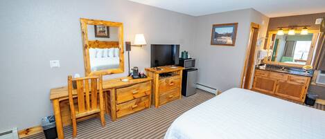 A hotel room with a bed, a wooden desk with a chair, a television, a lamp, and a mirror.
