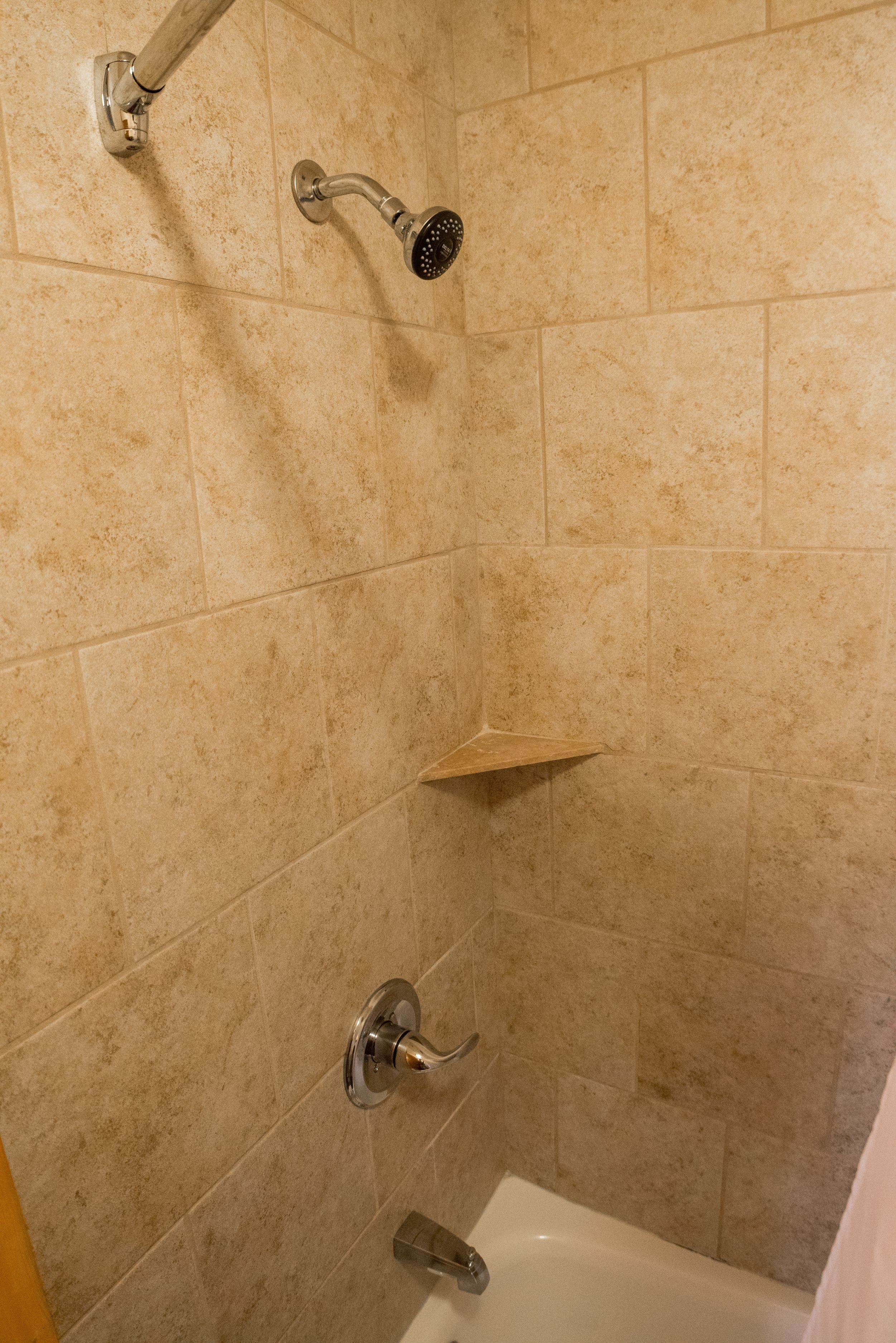 A shower with a handheld showerhead and a wall-mounted faucet.