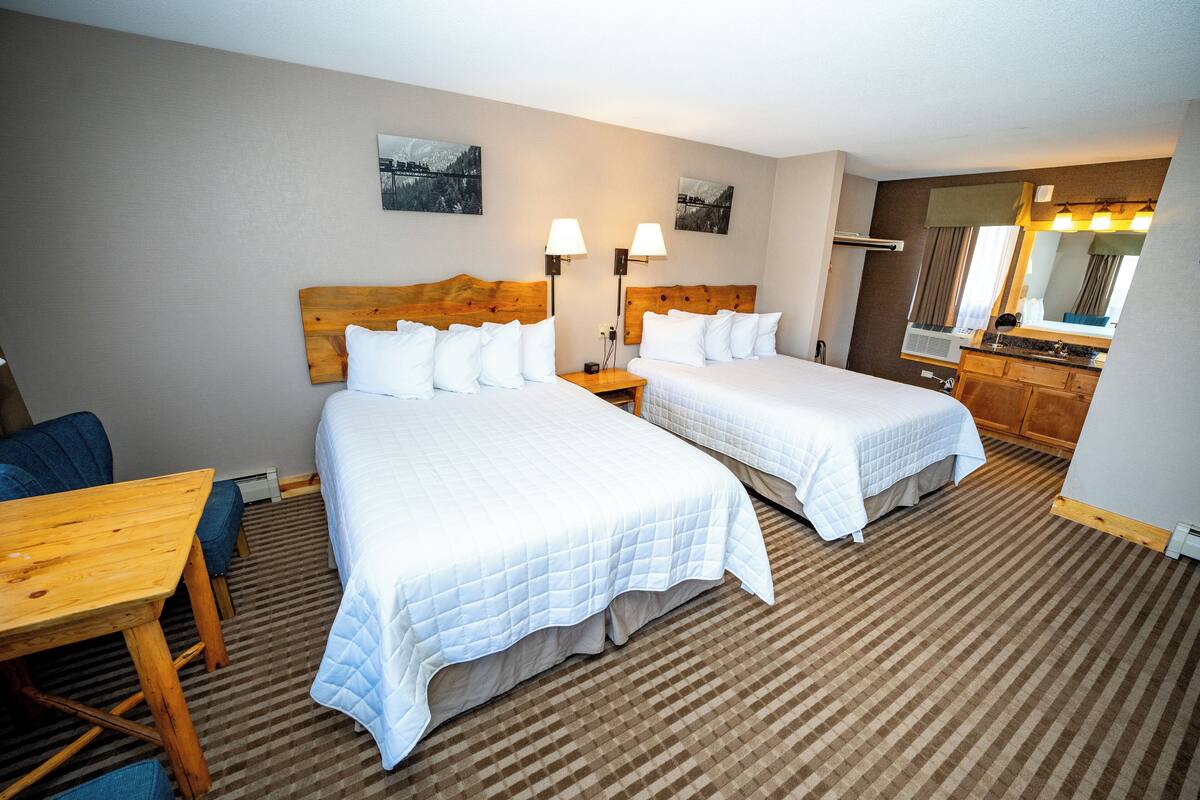 A hotel room with two beds, a wooden table, a desk, a chair, a dresser, and a mirror.