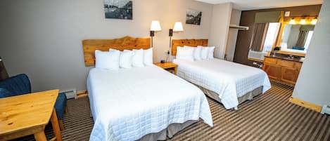 Habitación de hotel con dos camas, una mesa de madera, un escritorio, una silla, un aparador y un espejo.