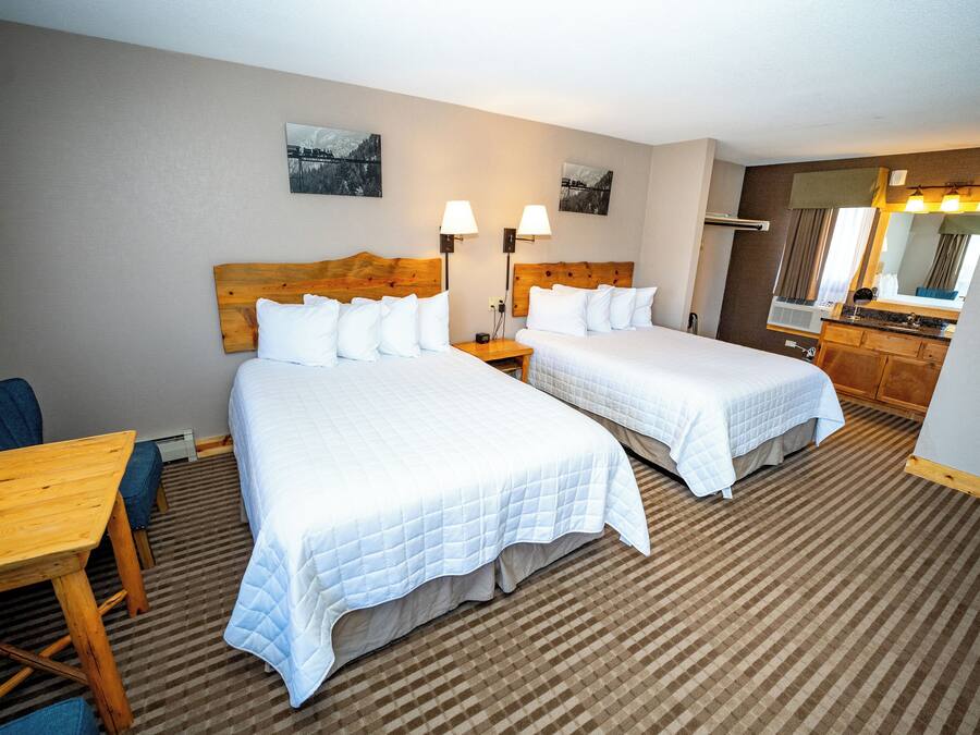 A hotel room with two beds, a wooden table, a desk, a chair, a dresser, and a mirror.