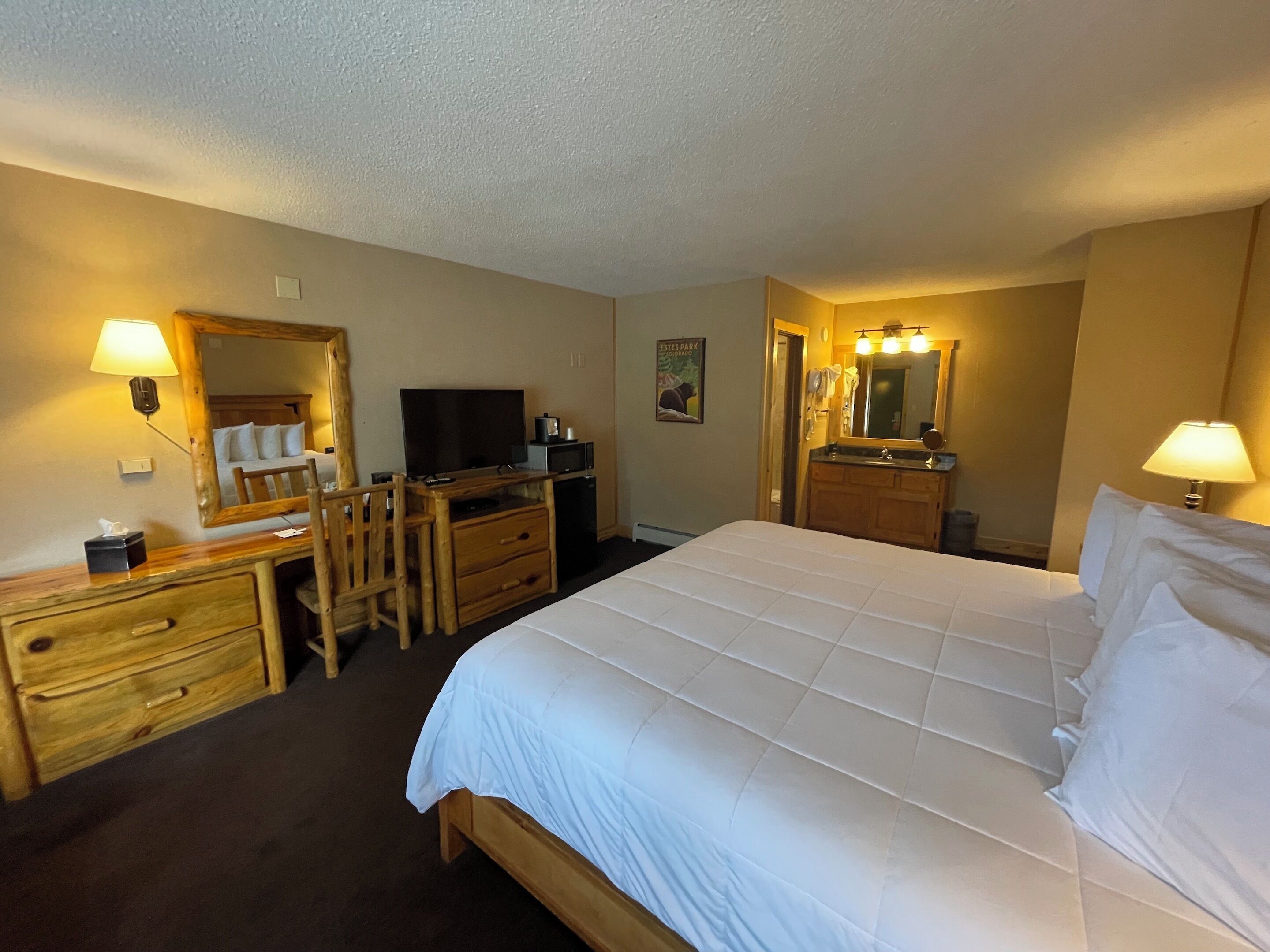 Une chambre d’hôtel comprenant un lit, un bureau avec un ordinateur, une télévision, un miroir et une salle de bain avec un lavabo et un miroir.