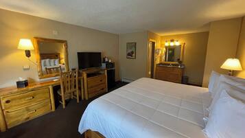 A hotel room with a bed, a desk with a computer, a television, a mirror, and a bathroom with a sink and mirror.