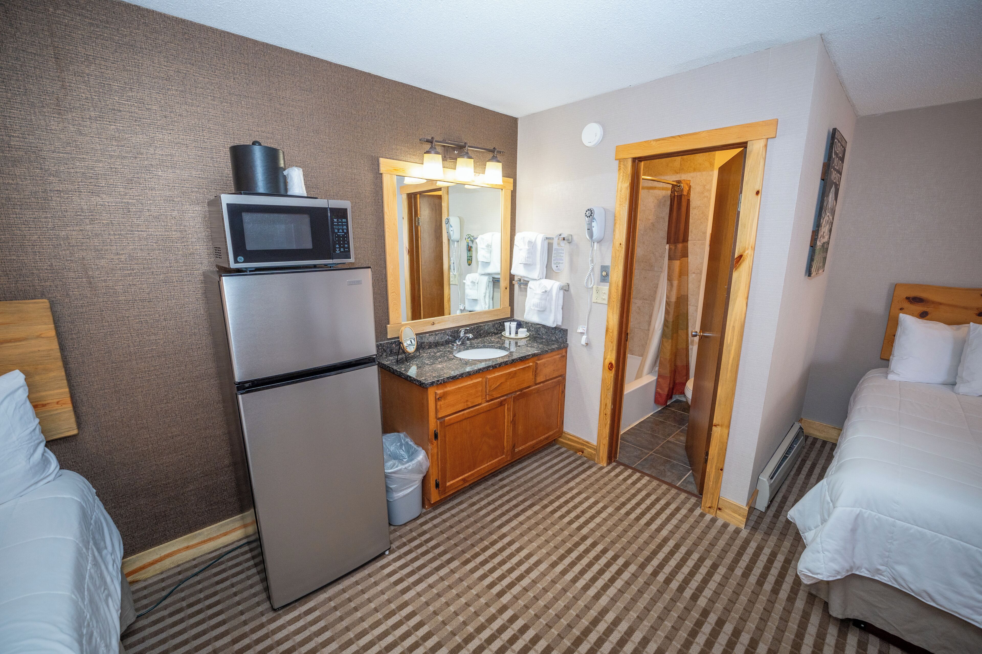 A hotel room with a refrigerator, microwave, sink, and a large mirror.