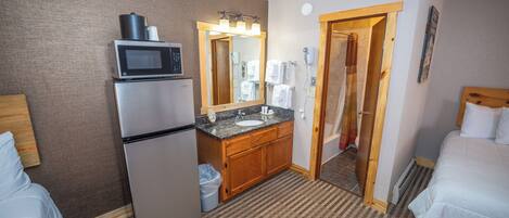 A hotel room with a refrigerator, microwave, sink, and a large mirror.