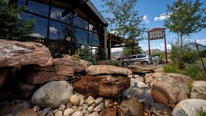 A modern building with a glass facade, a sign reading "HOTEL ESTES," and a natural landscape with rocks and trees. - Hotel Estes (Estes Park)