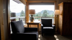 A cozy room with a view of mountains, two armchairs, a table with a lamp, and a wooden cabinet. - Hotel Estes (Estes Park)