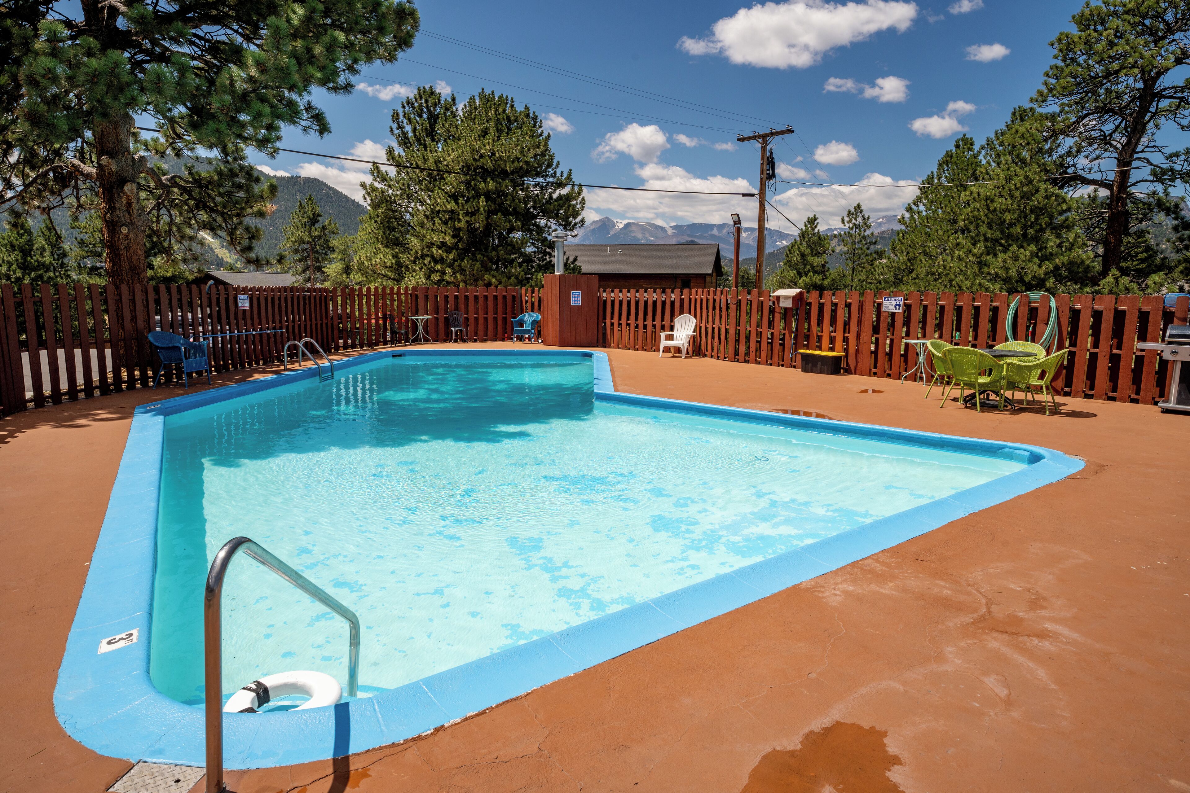 Ein rechteckiger Pool mit Metallleiter, umgeben von einem Holzzaun, im Hintergrund Stühle und ein Grill.