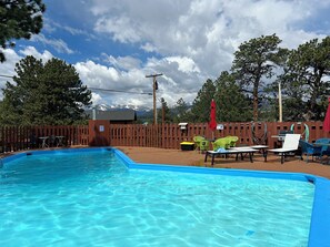 Una piscina con agua azul cristalina, rodeada por una valla de madera, y mobiliario exterior con sombrillas.