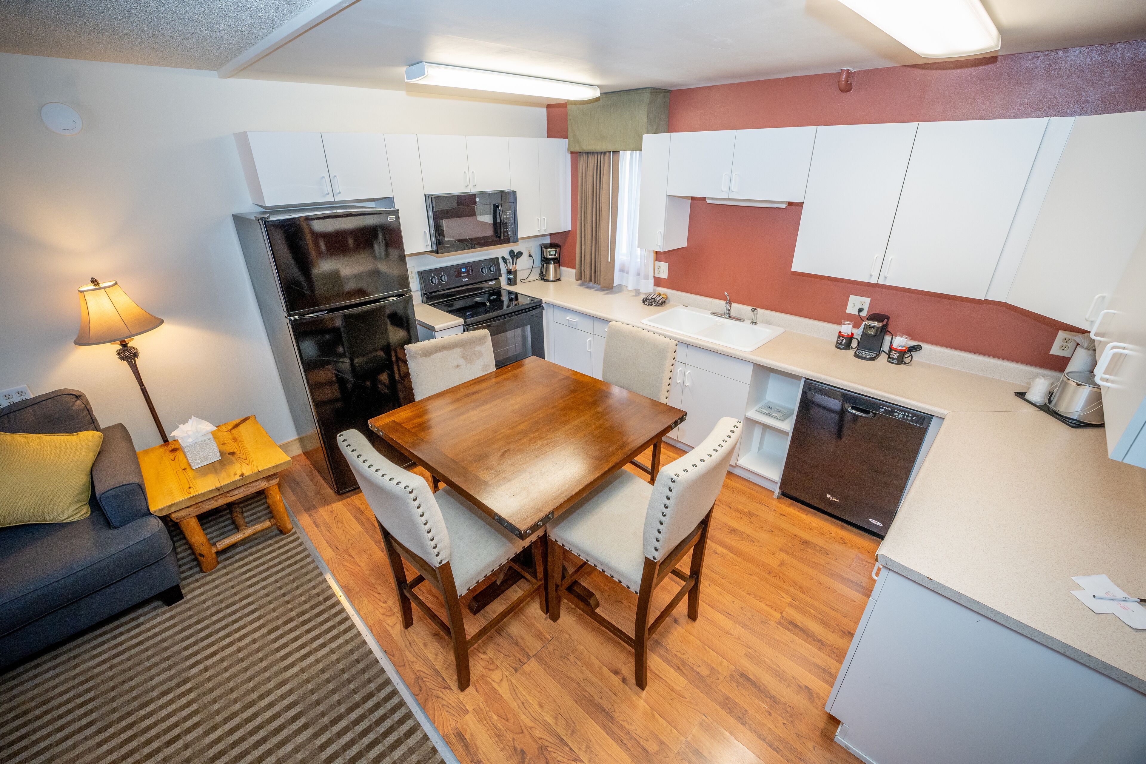 A compact kitchen with white cabinets, a wooden dining table, and a built-in dishwasher.