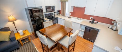 A compact kitchen with white cabinets, a wooden dining table, and a built-in dishwasher.