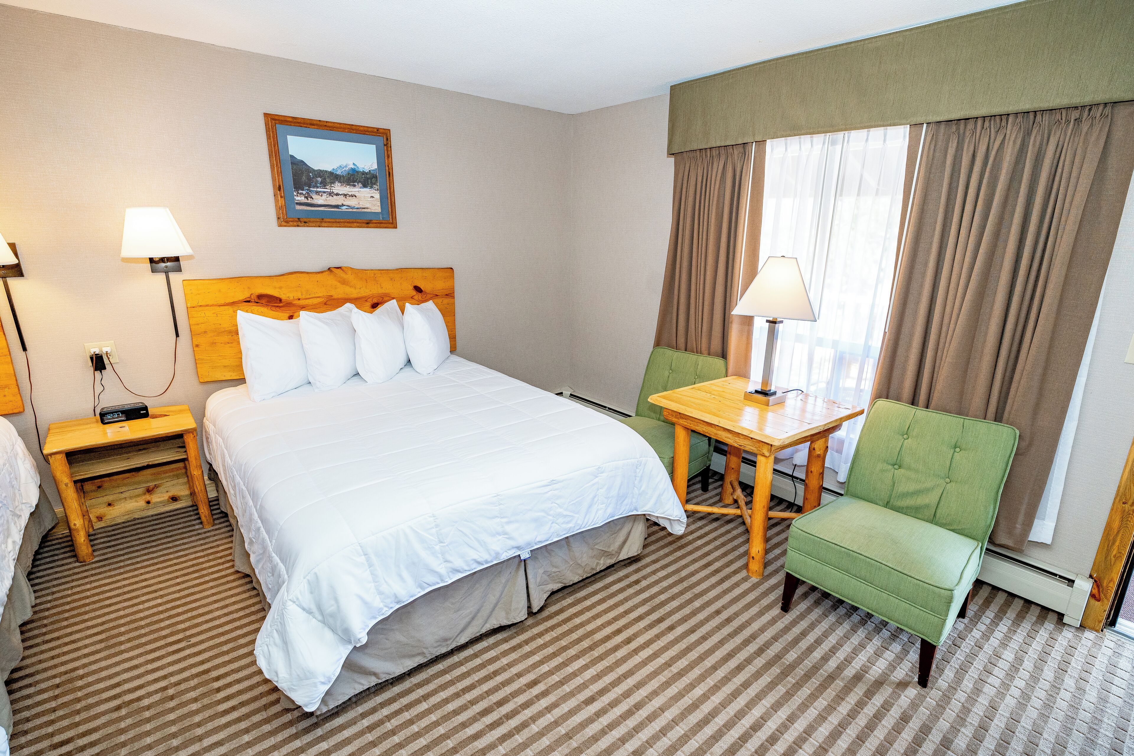 A hotel room with a large bed, a green armchair, a small table, and a painting on the wall.