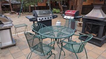 Un patio al aire libre con una mesa redonda de metal y cuatro sillas, rodeado por una parrilla y un estufa de leña.