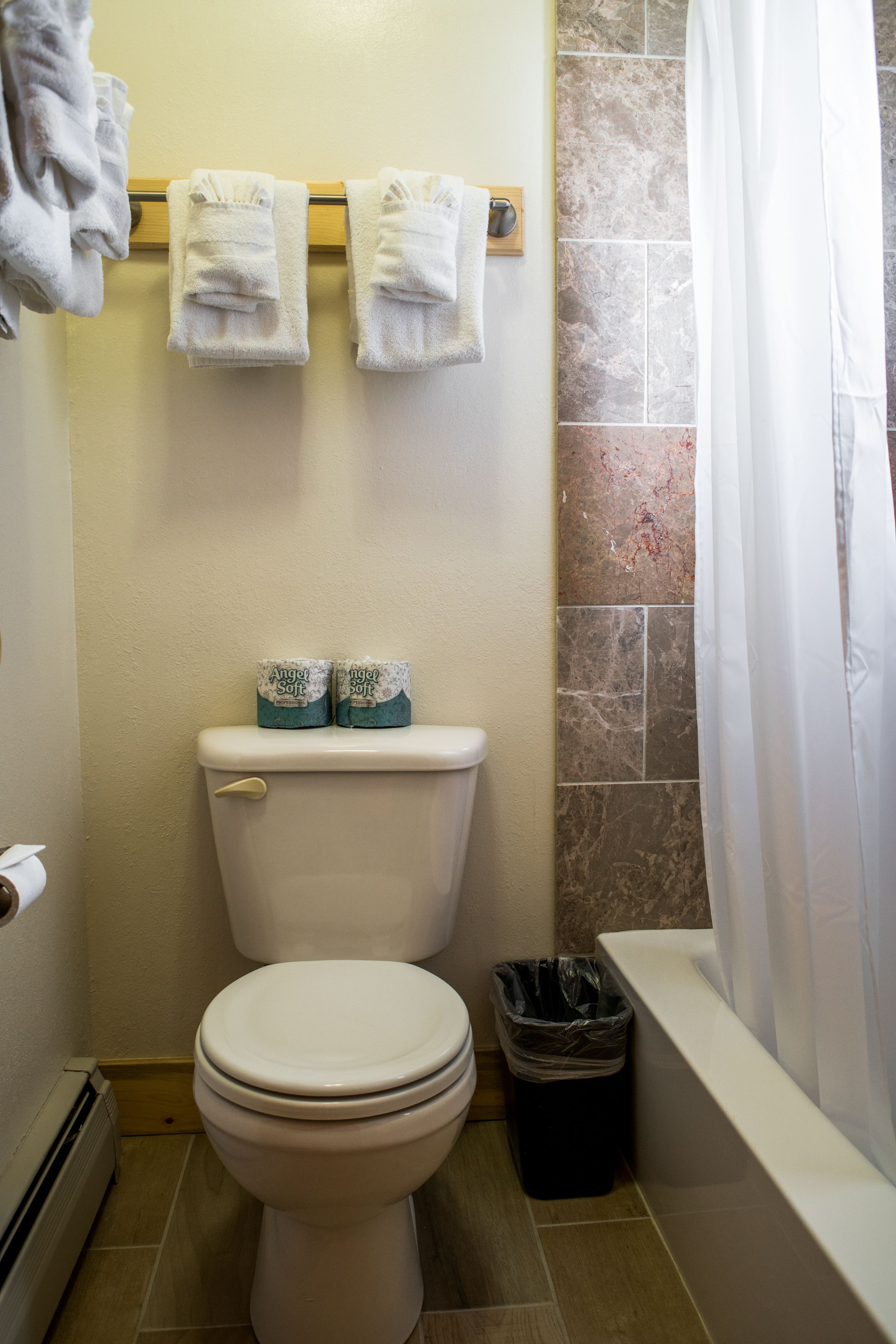 A bathroom with a toilet, two rolled-up towels on a rack, a trash bin, and a shower curtain.
