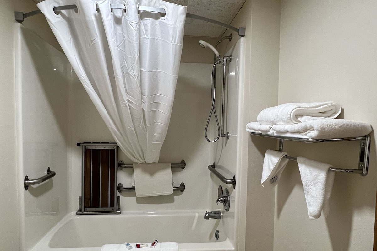 A bathroom with a bathtub, shower, and a towel rack with folded towels.