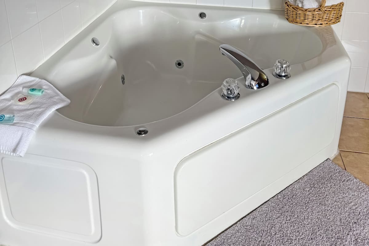 A white bathtub with a chrome faucet, a small glass bottle, and a white towel on the side.