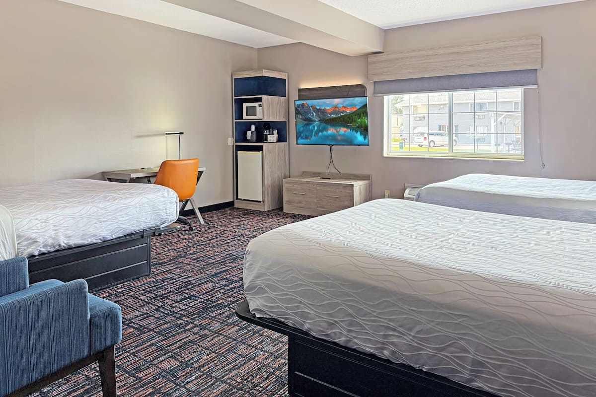 A hotel room with two beds, a desk, a chair, a TV, a microwave, and a window with a view of buildings.