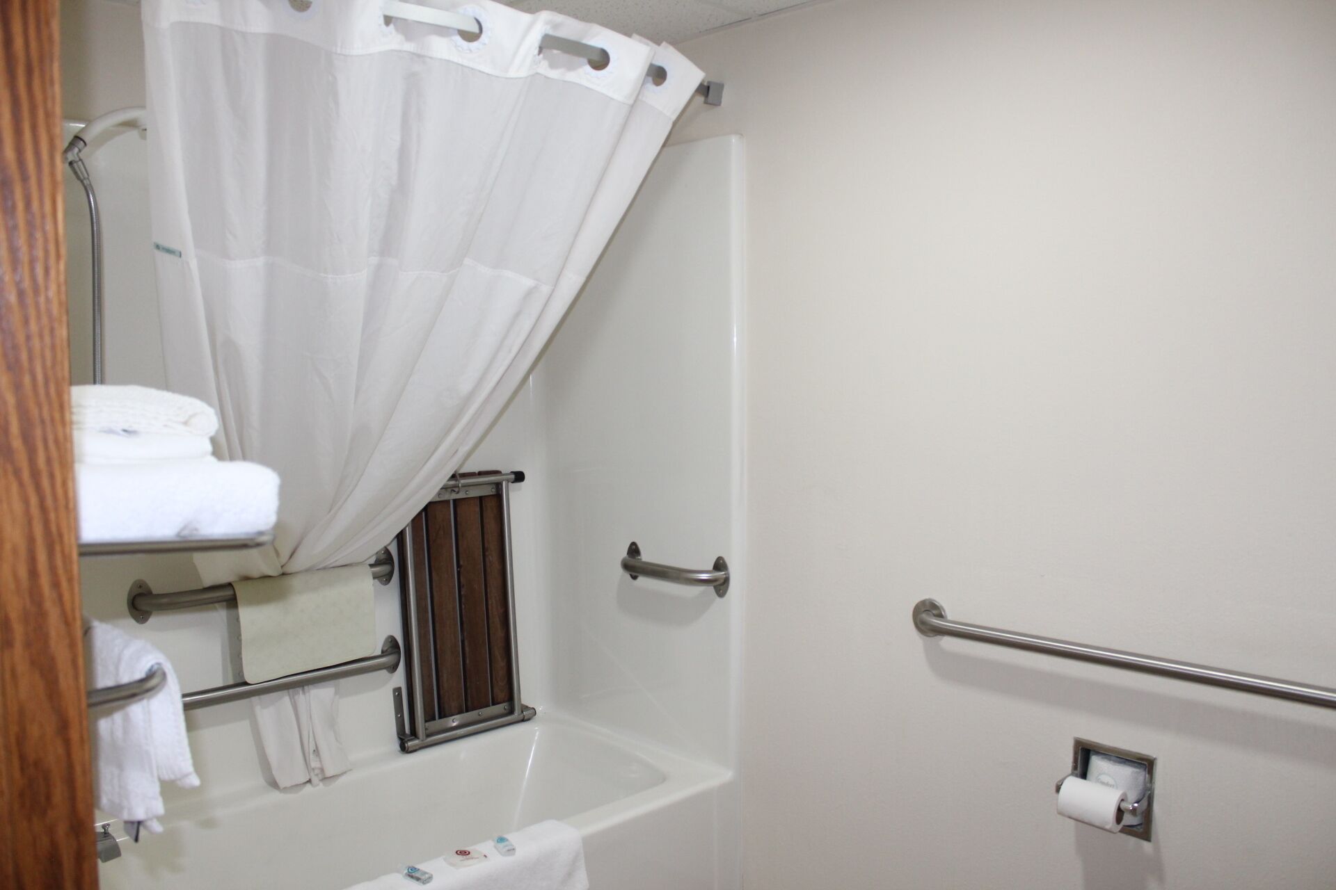 A bathroom with a shower curtain, a towel rack, a grab bar, and a toilet paper holder.