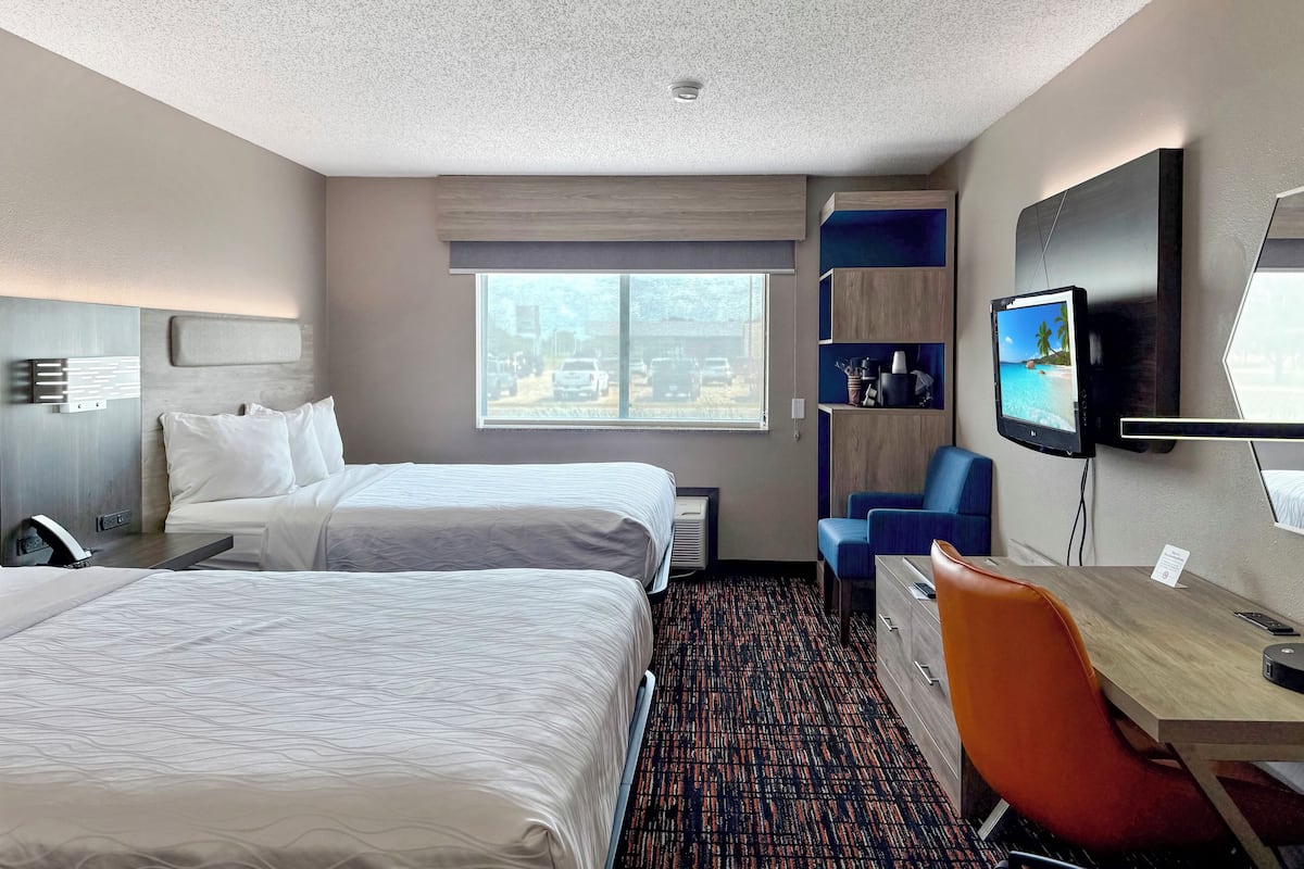 A hotel room with two beds, a desk, a chair, a TV, and a window with a view of the outside.