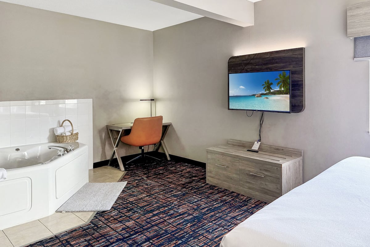 A hotel room with a bed, a desk with a chair, a TV mounted on the wall, a bathtub, and a small bathroom area.