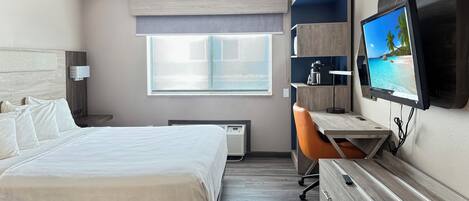 Habitación de hotel moderna con una cama grande, un escritorio, una silla, un televisor y una ventana con vista a la playa.