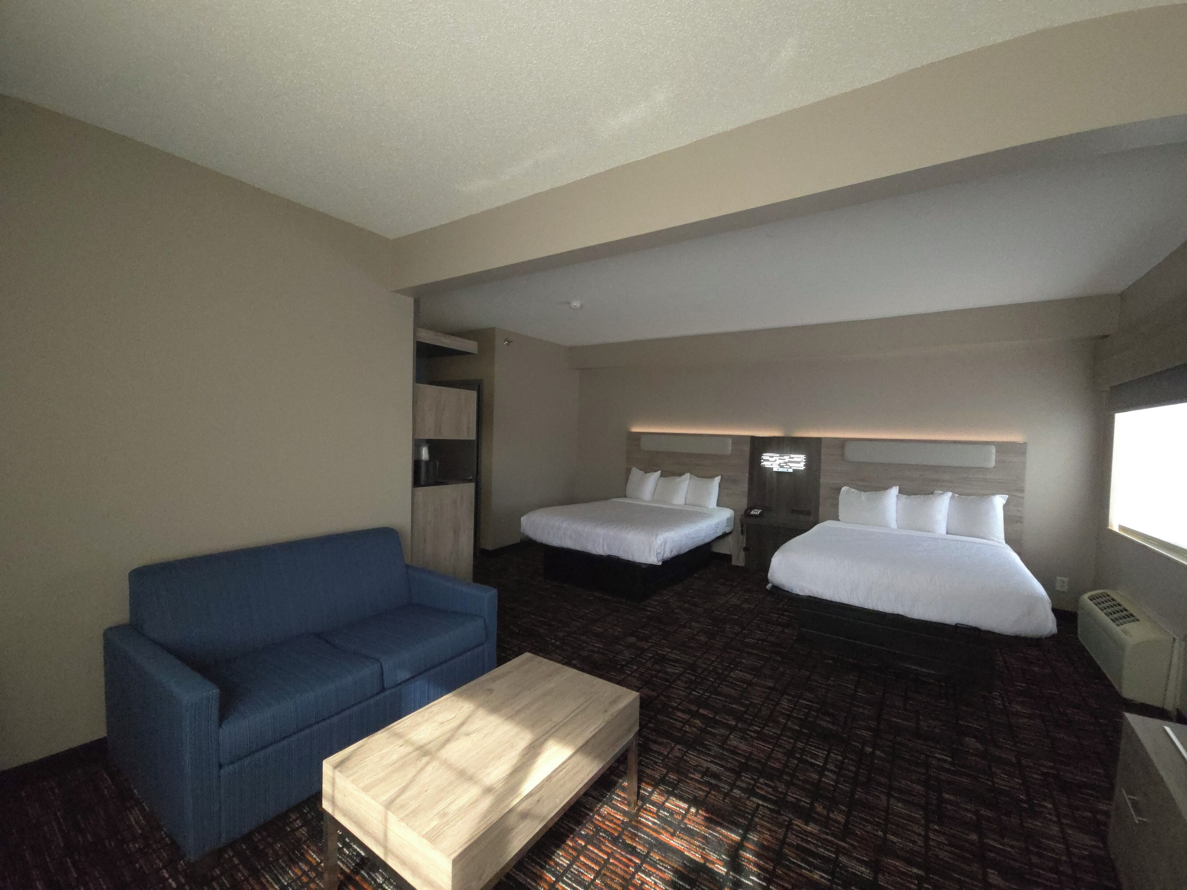 A hotel room with two beds, a blue sofa, a wooden coffee table, and a minibar.