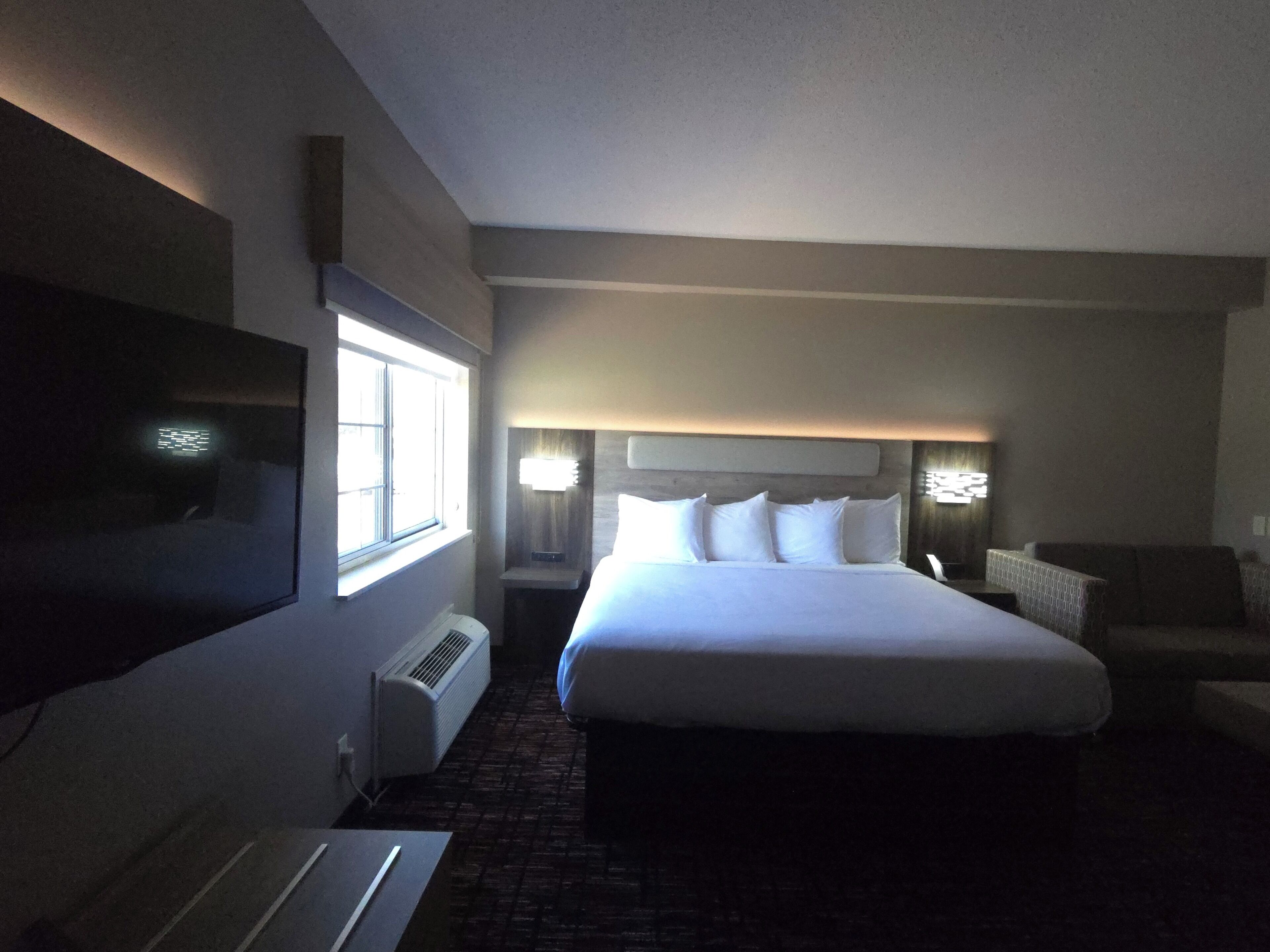 Une chambre d’hôtel dotée d’un grand lit, d’un téléviseur à écran plat, d’une fenêtre et d’un coin salon avec un fauteuil.