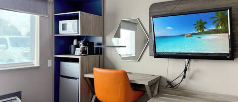 Habitación de hotel con cama, escritorio con silla, televisor en la pared, microondas, cafetera y refrigerador.