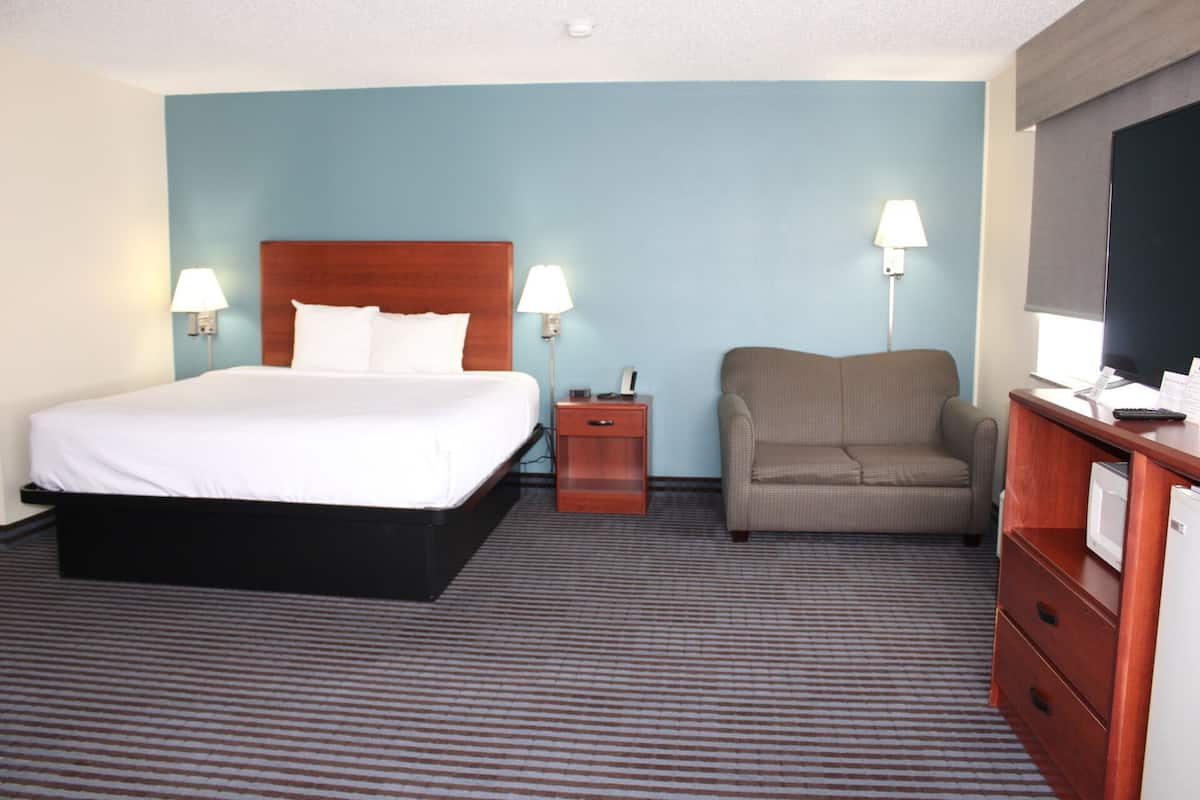 A hotel room with a bed, a chair, a desk with a computer, and two bedside lamps.